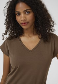 T-shirt marrone a V con maniche corte realizzato in tessuto morbido. La vestibilità è rilassata, evidenziando una texture liscia senza fantasie o decorazioni.