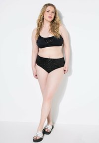 Set di bikini nero composto da un top elegante con dettagli scintillanti e uno slip a vita alta decorato con paillettes nere. Sandali bianchi con suole nere.