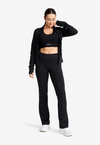 Svart idrottsklädsel med en åtsittande sport-bh, zip-up jacka och högmidjade byxor. Materialet verkar slätt med en stilren design.