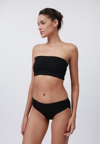 Crna rebrasta bandeau majica s nabranim detaljima, uparena s odgovarajućim bikinijem visokog struka. Glatka tekstura, minimalistički dizajn, uski kroj.