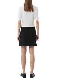 Witte geribbelde T-shirt met korte mouwen gecombineerd met een zwarte A-lijn rok. De outfit heeft een gladde textuur en een strakke silhouet. Zwarte schoenen maken de look compleet.