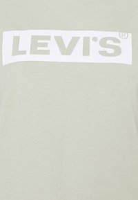 Ljust grön t-shirt med en mjuk textur som har en stor vit "LEVI'S" logotyp i en rektangulär grafik på framsidan.