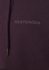 Lynlås hættejakke i mørk lilla stof, med en struktureret overflade og mærkenavnet "RESTERÖDS" i præget skrift på forsiden.
