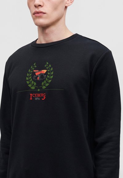 Homme portant un sweat-shirt noir avec un graphisme rouge et vert et le texte Iceberg 1974 sur la poitrine