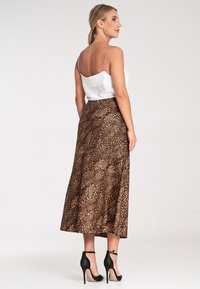 Spódnica midi w wzór lamparta o swobodnym kroju, wykonana z materiału przypominającego satynę. Połączona z dopasowaną białą bluzką i czarnymi szpilkami.