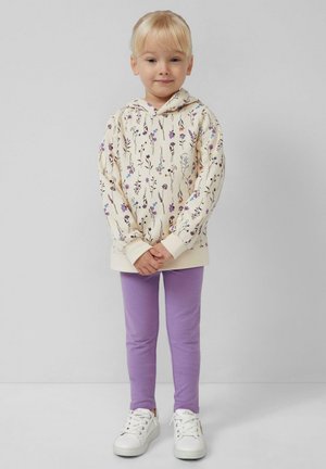 Beige hoodie met bloemmotief, paarse leggings en witte sneakers. Hoodie heeft een voorzak en ribgebreide manchetten.