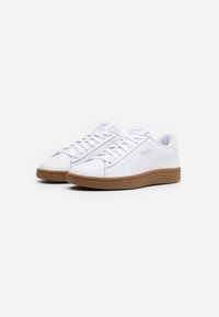 Un paio di sneakers bianche Puma con suole in gomma, allacciate, angolate a sinistra su uno sfondo bianco semplice.