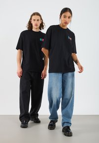 Black oversized t-shirts with front logos, paired with dark and light baggy jeans. Both wear black shoes. Simple and casual design.
