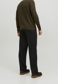 Maglione a maglia verde oliva abbinato a pantaloni neri. Il maglione presenta un collo rotondo e maniche lunghe; i pantaloni hanno una vestibilità morbida e gambe dritte.