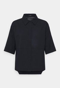 Blouse noire à manches courtes en texture avec col pointu, patte de boutonnage dissimulée et ourlet arrière légèrement plus long.