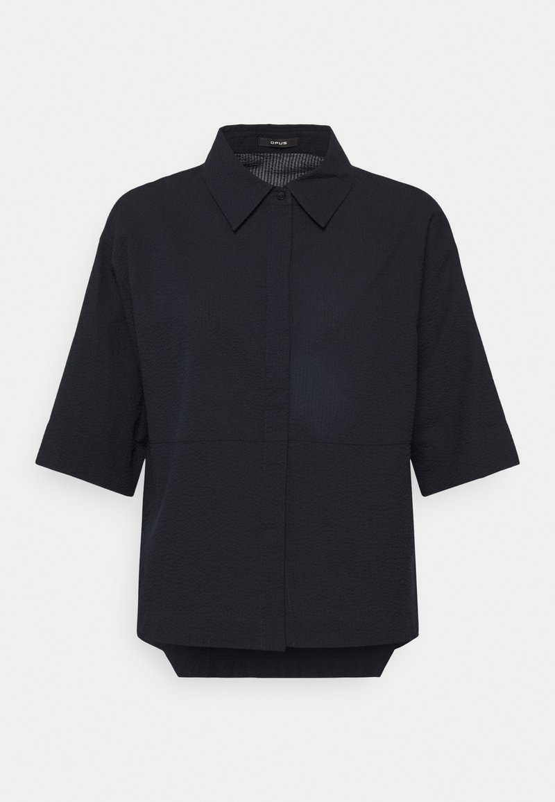 Blouse noire à manches courtes en texture avec col pointu, patte de boutonnage dissimulée et ourlet arrière légèrement plus long.