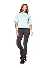 Jasnozielona krótki T-shirt z krótkimi rękawami, w zestawie z ciemnoszarymi dopasowanymi legginsami. Czarne buty na platformie z jasnobrązowymi podeszwami.