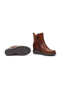Bottines en cuir marron avec une fermeture éclair sur le côté et des détails de sangle, dotées d'une semelle en caoutchouc texturée. Fini lisse avec des accents de couture subtils.