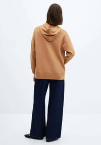 Sudadera con capucha marrón hecha de material suave, de corte holgado, combinada con jeans de mezclilla oscuros de pierna ancha, vista desde la parte de atrás.