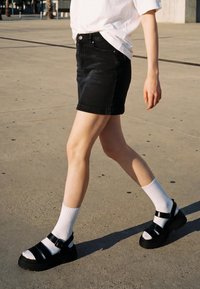 Personne marchant à l'extérieur portant une jupe en jean noire, des chaussettes blanches, des sandales à plateforme noires et un t-shirt blanc.