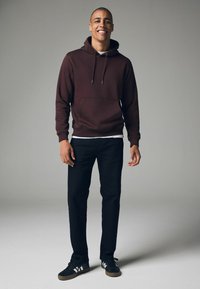 Sudadera con capucha de color burdeos con un bolsillo frontal, combinada con pantalones negros y zapatillas negras con rayas blancas. Textura suave, diseño casual.