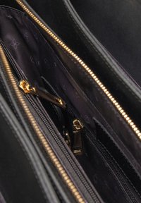 Zwart leren handtasinterieur met gouden hardware, meerdere ritssluitingen en een donkere voering met een subtiel patroon.