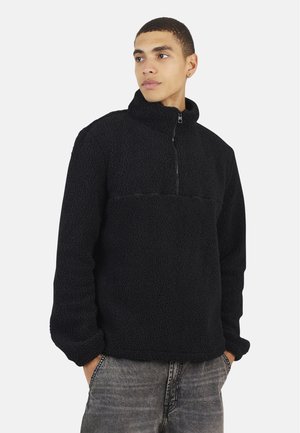 Veste polaire noire à col montant et zip quart, dotée d'un tissu épais et texturé ainsi que d'une coupe décontractée.