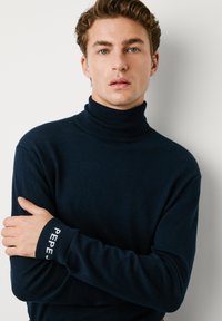 Jūrinis golfas, pagamintas iš minkštos medžiagos, su briaunotu kaklu ir rankogaliais, puikuojantis baltu „PEPE“ tekstu. Prigludęs dizainas, minimalistiškas stilius.