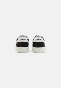 Czarno-białe sneakersy Levi's z teksturowaną białą podeszwą, wyściełanym kołnierzem i wyraźnym logo na pięcie. Klasyczny design typu low-top.