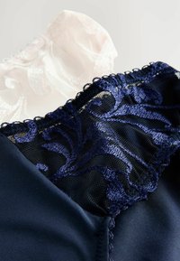 Material de marina cu dantelă și broderie florală suprapune un strat subțire de roz deschis; textura netedă contrastează cu detaliile intricate.