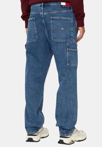 Jeans cargo in denim blu con diverse tasche, vestibilità rilassata e dettagli di cucitura in vista, indossati con sneakers color crema.