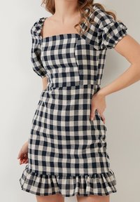 Figurformad klänning i marinblått och krämfärgat rutmönster, med fyrkantig halsringning, puffärmar och volangslut.