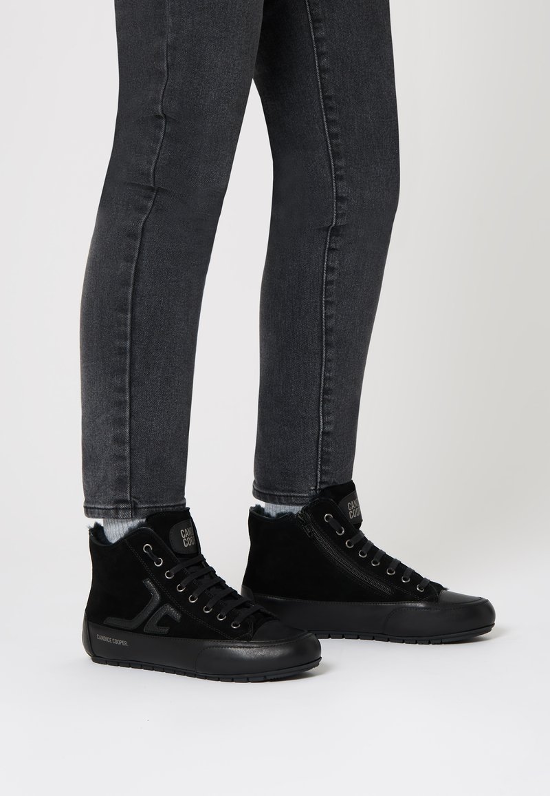 Black high-top sneakers made of suede and synthetic material, featuring laces, a side zipper, and a logo on the tongue. Rubber sole.