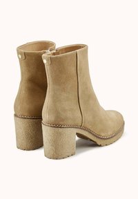 Bottines en daim beige avec bout arrondi, talon épais texturé et couture décorative autour de la semelle, dotées d'une fermeture éclair latérale.