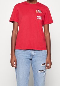 Camiseta de algodón roja de manga corta, con un bolsillo en el pecho que presenta el texto "FELIZ NAVIDAD" y un detalle gráfico de Papá Noel.