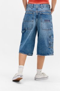 Pantalones cortos cargo de mezclilla en azul claro con un corte holgado. Presentan múltiples bolsillos y detalles de costura en la parte trasera, combinados con zapatillas blancas.