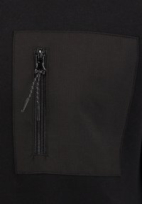 Sudadera negra con un parche texturizado y un bolsillo con cremallera negra. El bolsillo tiene una cremallera plateada y un fondo de tela suave.