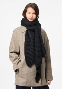 Sort ribbet tørklæde lavet af blødt, tekstureret stof, der smukt hænger om halsen, parret med en beige frakke og synlige lommer.