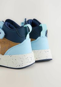 Las zapatillas en azul y marino presentan un diseño texturizado con una suela blanca moteada. Incluyen acentos en azul claro y detalles en cuero marrón.