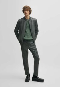 Gray bomber jacket over a green ribbed sweater, paired with gray checkered trousers and black loafers. Smooth fabric with subtle texture.