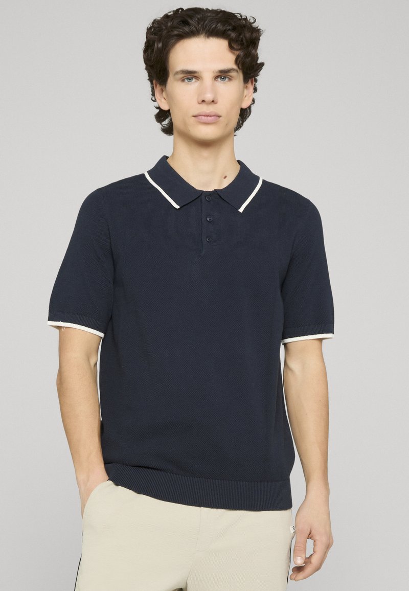 Polo bleu marine à manches courtes avec un motif texturé, col blanc et accents aux manches, et patte de boutonnage à trois boutons. Ourlet côtelé.