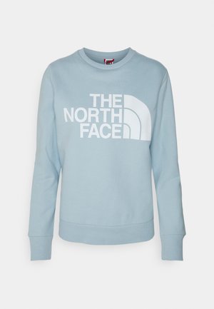 Sweat-shirt bleu clair à manches longues et col rond avec logo blanc "THE NORTH FACE" et motif en quart de cercle sur le devant.