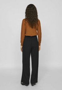 Chemise marron à manches longues associée à un pantalon noir à jambes larges. L'ensemble présente une texture douce et une coupe décontractée avec une taille élastique.