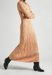 Stickad maxiklänning i orange med ribbad textur, med långa ärmar och rundad halsringning. Matchas med svarta cowboystil-ankelstövlar.