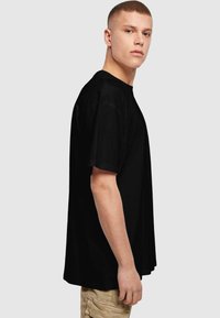Black short-sleeve t-shirt made of cotton. Loose fit with a rounded neckline and side seams. Minimalist design, no visible patterns or graphics.