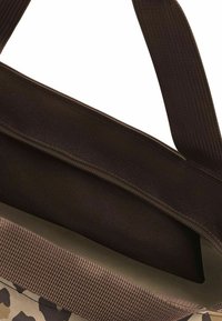 Brown canvas bag interior with a smooth fabric lining. Features a brown strap and zipper detail. Camo pattern on the outer surface.