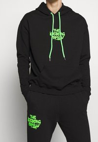 Svart huvtröja med neongröna dragsnören och logotyp. Har en framficka, ribbade ärmar och matchande svarta byxor med logotyp.