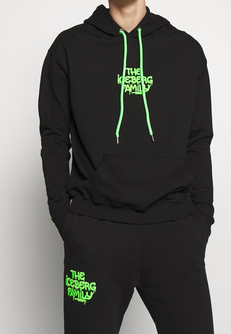 Svart huvtröja med neongröna dragsnören och logotyp. Har en framficka, ribbade ärmar och matchande svarta byxor med logotyp.