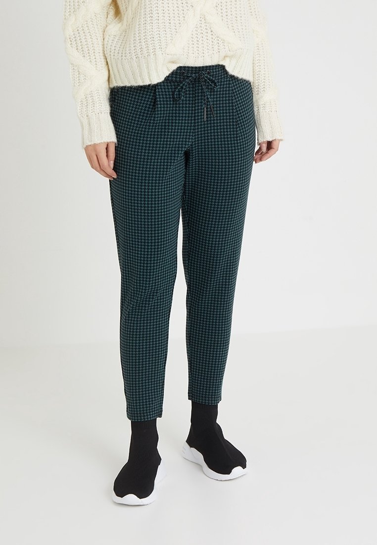 Pantalones de cuadros verdes con cintura ajustable, corte slim y textura sutil, combinados con zapatos negros sin cordones.