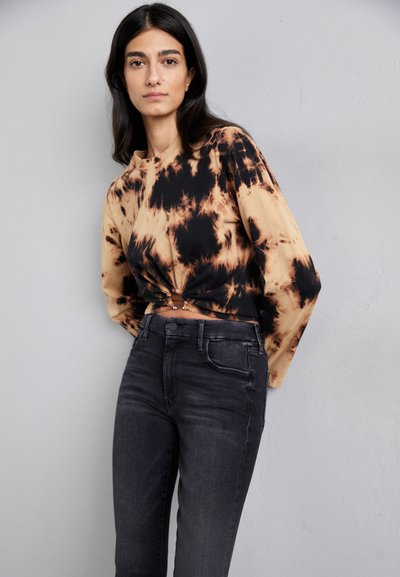Langermet, tie-dye topp i beige og svart med en knute detalj foran; kombinert med tettsittende sorte jeans. Glatt stofftekstur.