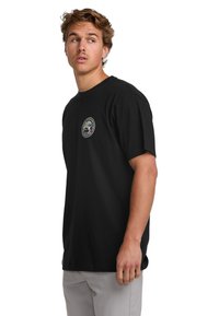 Black cotton t-shirt with short sleeves, featuring a circular logo on the chest. The design is simple and solid without patterns.