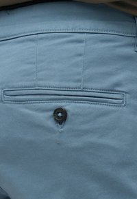 Ανοιχτό μπλε παντελόνι με πίσω τσέπη που κλείνει με μαύρο κουμπί. Το ύφασμα έχει απαλή υφή και λεία επιφάνεια.