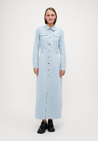 Dlhé, svetlomodré džínsy šaty s dlhými rukávmi, golierom, vreckami na hrudi a predným zapínaním na gombíky. Nosí sa s čiernymi topánkami.