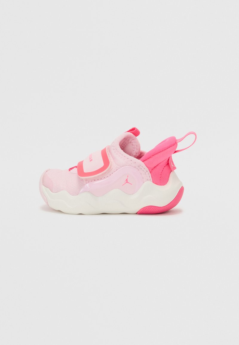 Chaussure de sport rose avec une texture lisse, semelle épaisse blanche, bande Velcro et boucle de traction. Présente une combinaison de couleurs rose et blanche avec un détail de logo.