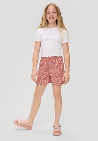 Haut blanc à manches courtes avec des bords festonnés, associé à un short floral rose et des sandales rose clair avec une semelle plus épaisse et des sangles ajustables.